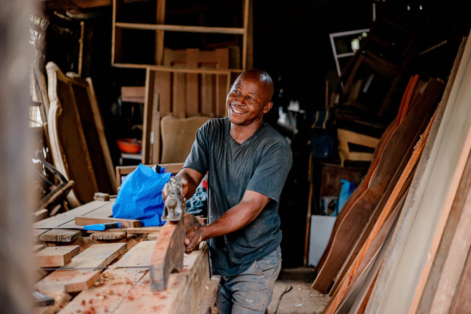 A smiling carpenter planing a length of wood in his workshop.